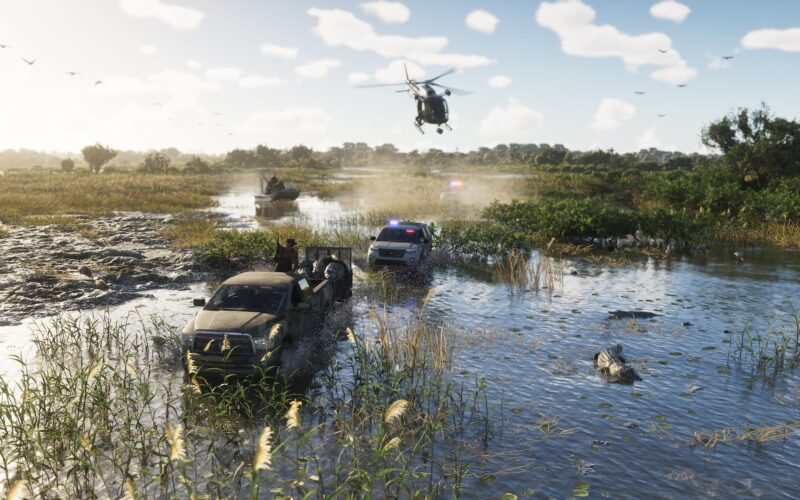 Official Grand Theft Auto VI image of a flooded marsh track where a pickup and a second vehicle drive through shallow water under a partly cloudy sky, with a helicopter overhead