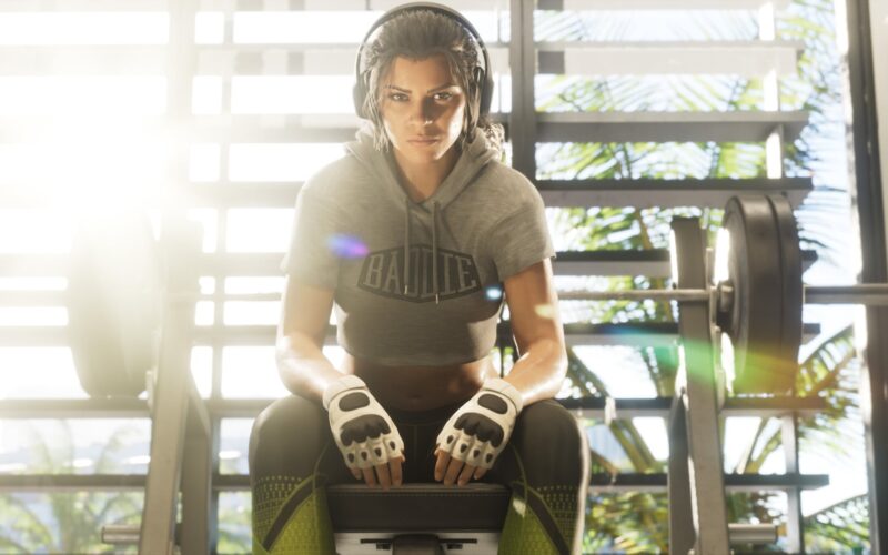 Official Grand Theft Auto VI image of Lucia Caminos sitting on a gym bench wearing headphones and fingerless gloves