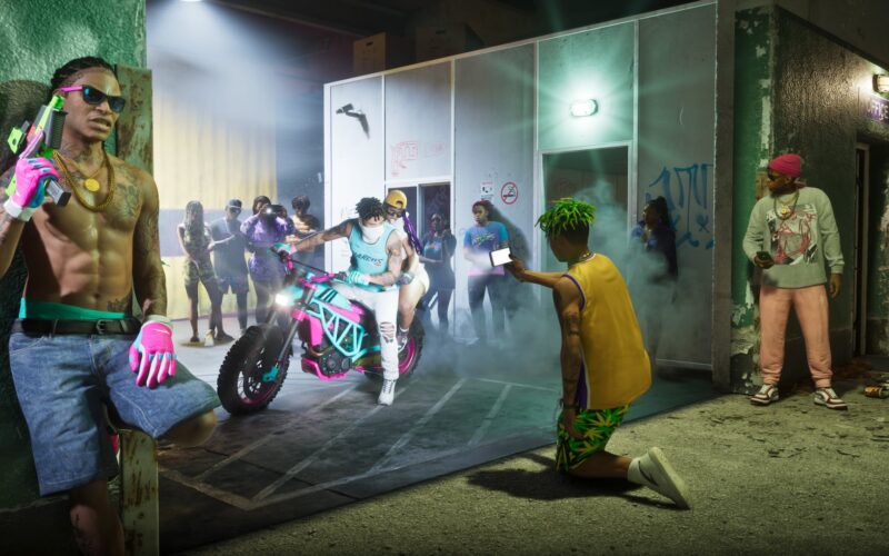 Official Grand Theft Auto VI image of onlookers filming two riders on a pink and teal motorbike in a smoky alley, with a man holding a gun leaning on the wall at left
