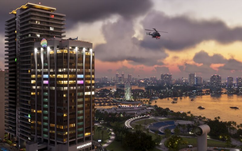 Official Grand Theft Auto VI screenshot of a Vice City waterfront at dusk, with a helicopter over a lit skyscraper and a Ferris wheel by the bay